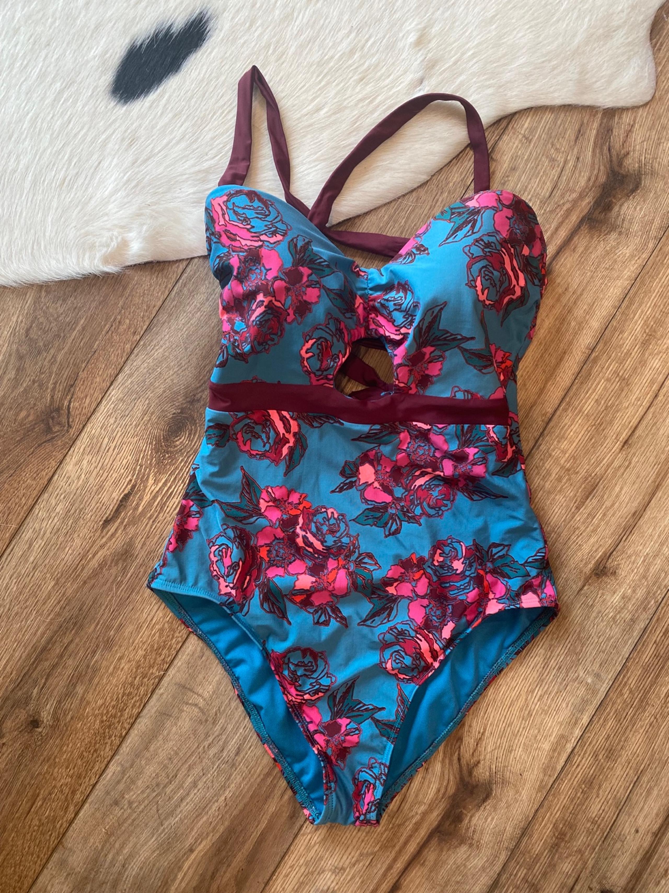 Basta Surf one-piece swimsuit with a teal background and a pink floral pattern