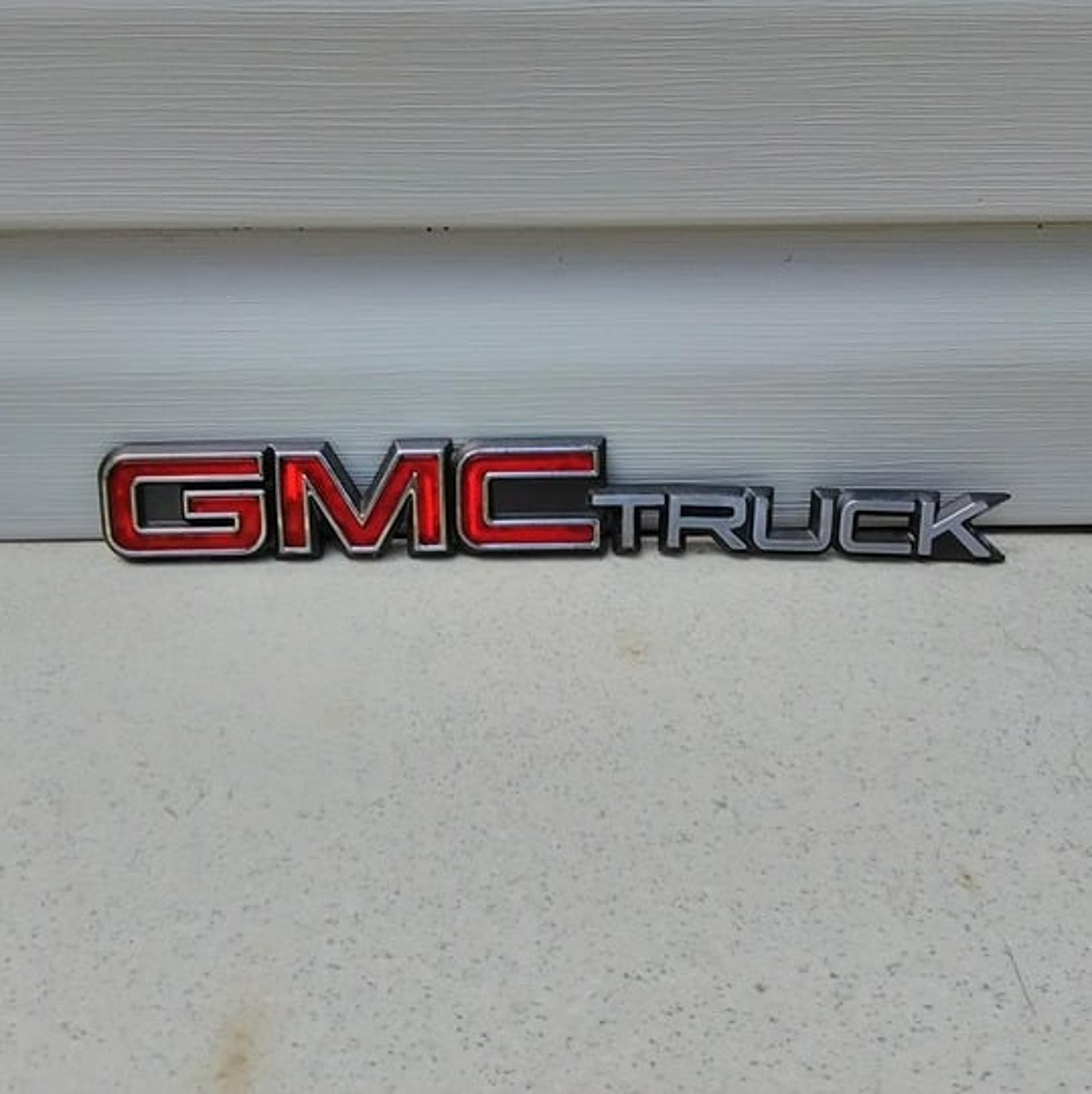 Used Truck red, chrome and charcoal plastic emblem. Good condition. - Gmc