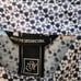 A white, short-sleeved polo shirt with navy floral print from the golf brand ZOY.
