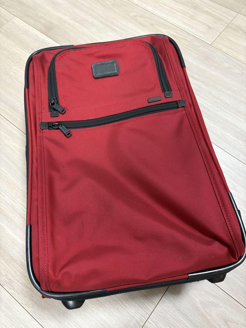 A red nylon TUMI carry-on suitcase.